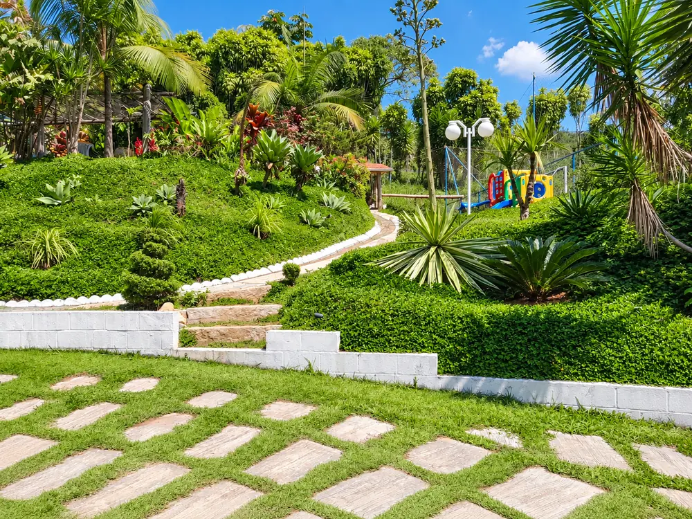 Jardim paisagístico em declive com caminho de pedra e playground ao fundo